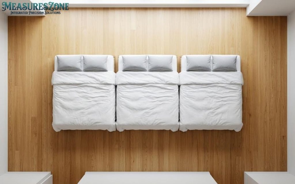 Top-down view of three minimalist beds with white duvets and grey pillows on a wood plank floor.
